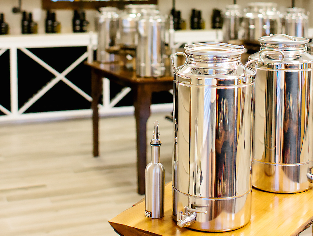 Large steel bins with dispensers—called “fustis”—house fresh oils and vinegars to sample at Season to Taste, an olive oil and balsamic vinegar tasting room that opened a few months ago on Highland Road. (Photo by Chelsea Caldwell)