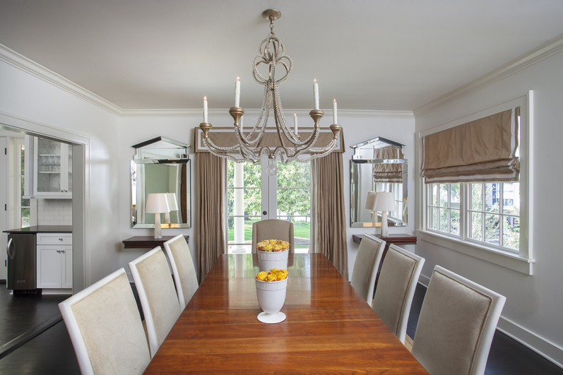 Contemporary upholstered chairs surround an antique table in the dining room. The Niermann Weeks chandelier features a classic style with rock crystal accents. Modern pediment mirrors above antique empire folding tables flank the double doors.