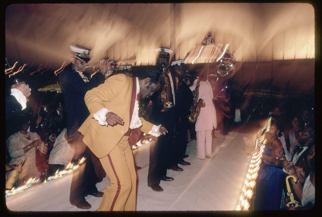 “Zulu Social Aid and Pleasure Club ball,” by Mitchel Osborne, depicts members of the Dejan’s Olympia Brass Band playing at a 1988 Mardi Gras ball. (THNOC; gift of Mitchel Osborne; 2007.0001.308 ©Mitchel Osborne)