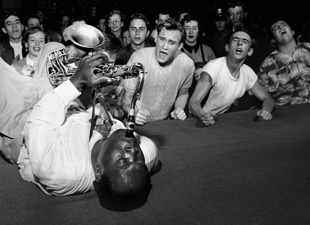A black and white photo by famous photographer Bob Willoughby that shows Big Jay McNeely driving the crowd into a frenzy during a show at Olympic Stadium in Los Angles CA circa 1951